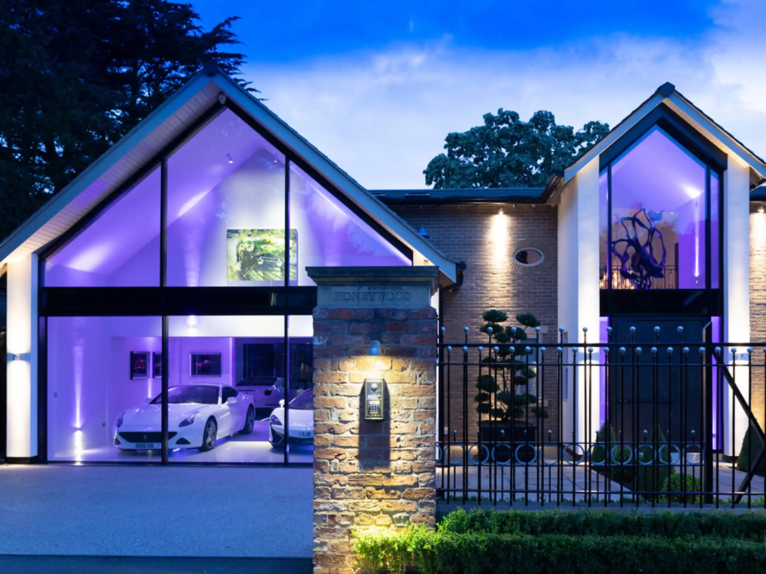 Illuminated glass-front garage in Alderley Edge showcasing luxury cars at night