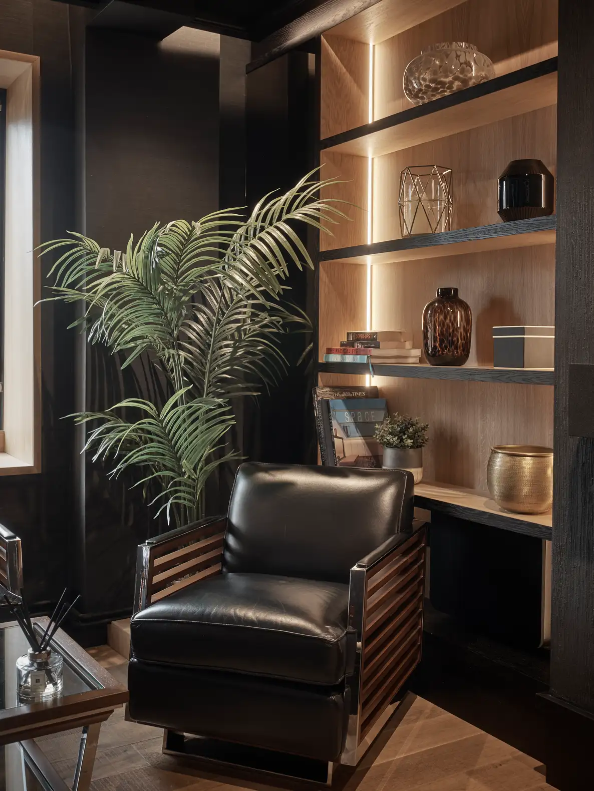 Black leather chair beside greenery and styled shelves in luxury office.